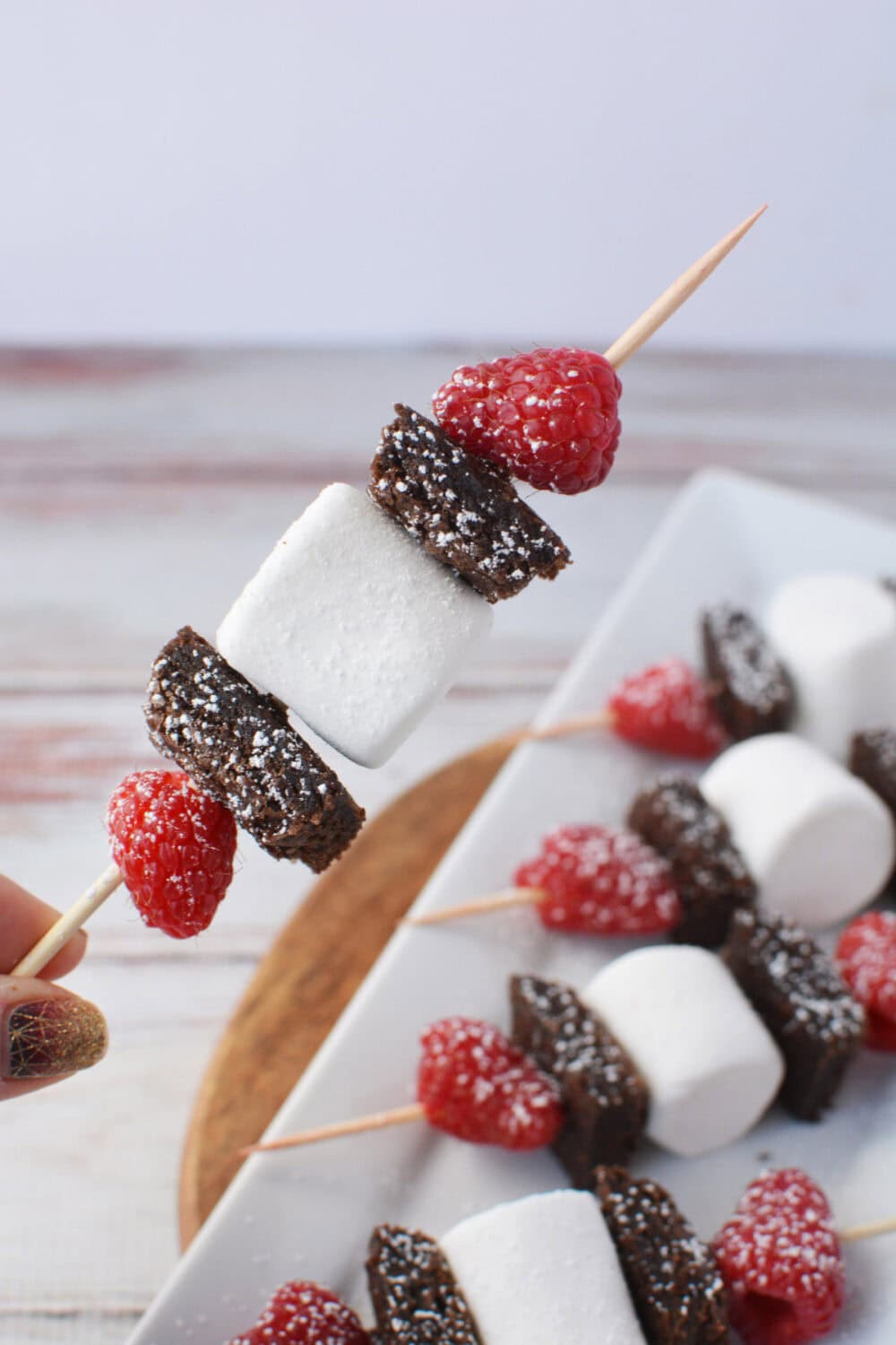 Holding a brownie, raspberry, marshmallow skewer. 