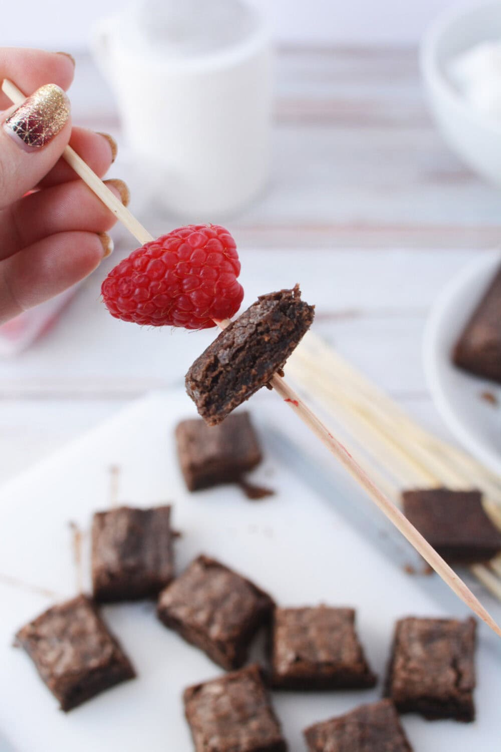 Brownie on a skewer next to a raspberry.