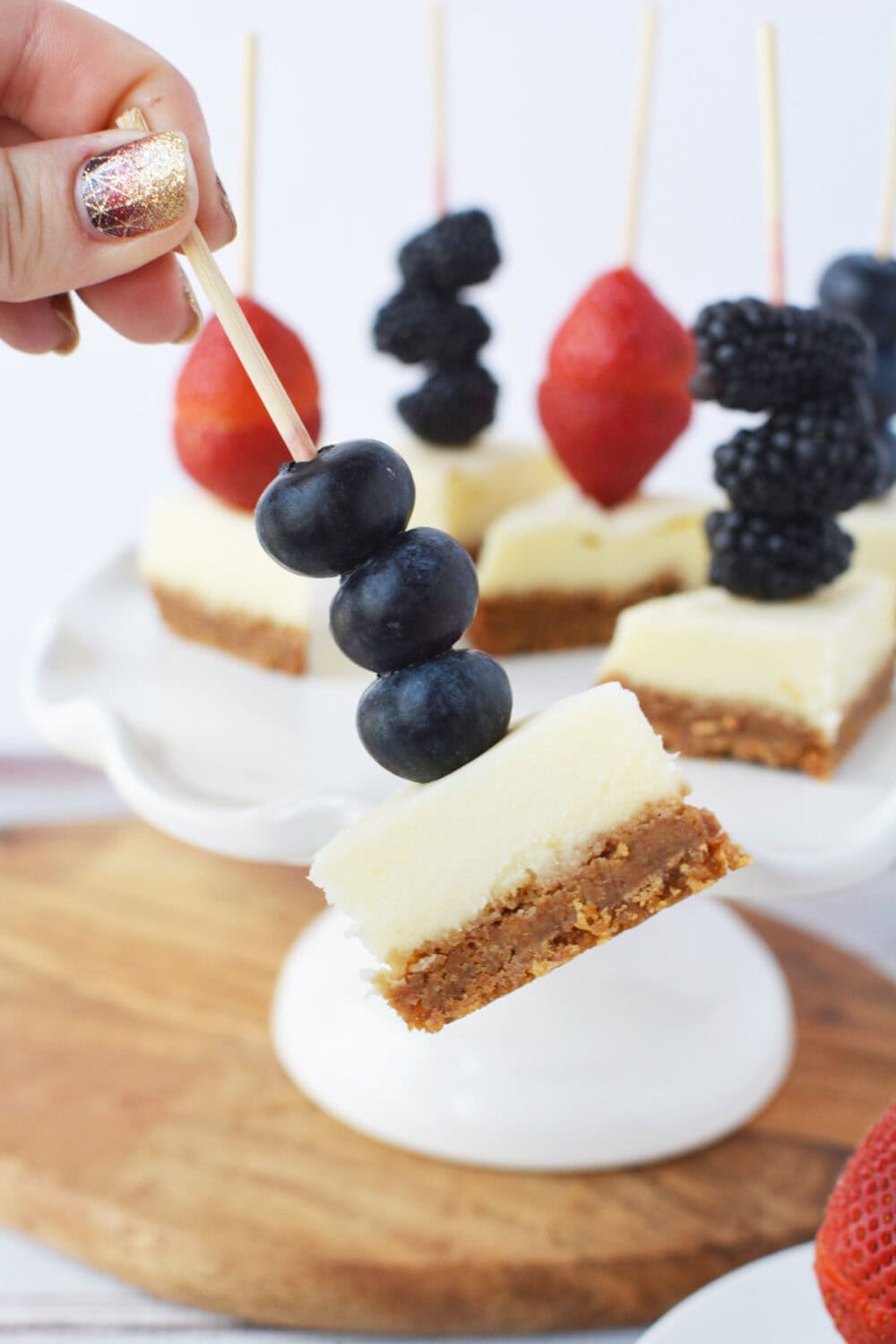 Three blueberries on a skewer with a cheesecake bite.