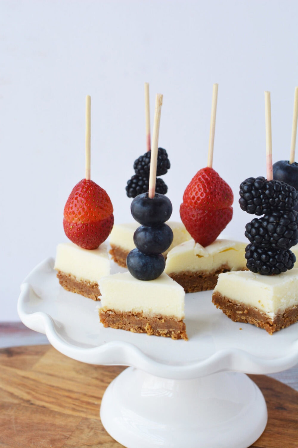 Berry cheesecake skewers on a white serving tray.