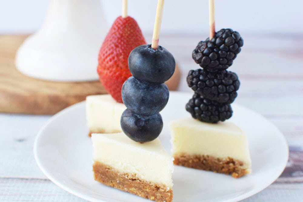 Cheesecake bites on skewers with strawberries, blueberries, and blackberries. 