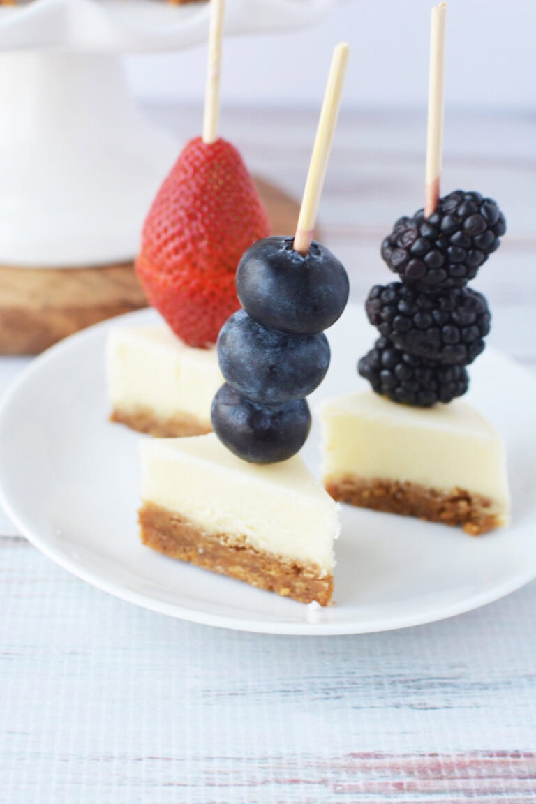 Three berry cheesecake skewers on a plate.