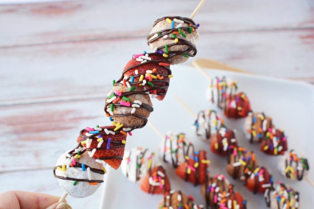 Holding a donut hole skewer with chocolate drizzle and sprinkles.