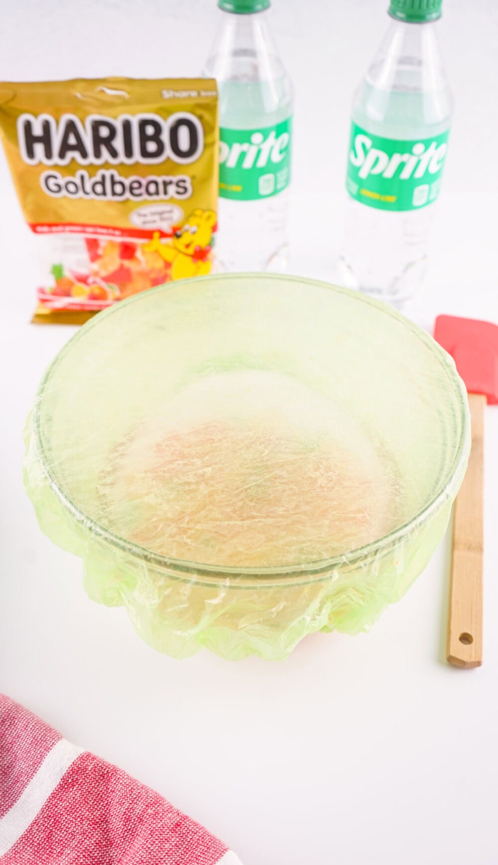 Bowl of gummy bears and Sprite covered with plastic wrap.