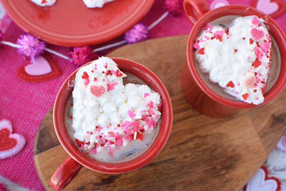 Heart whipped cream toppers in red mugs of hot cocoa. 