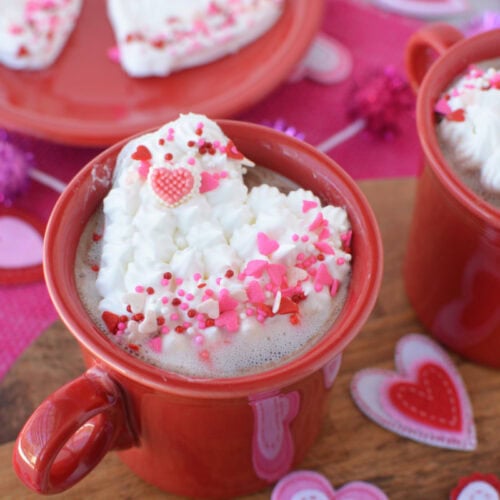 Whipped cream shaped in hearts on top of mugs of hot cocoa.