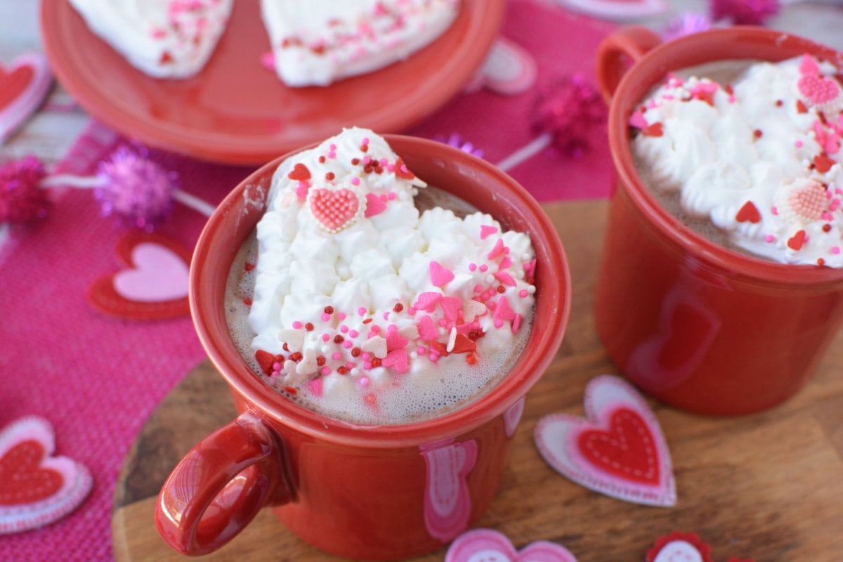 Whipped cream shaped in hearts on top of mugs of hot cocoa.