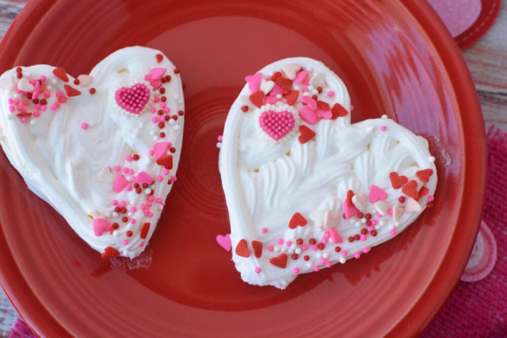 Two heart whipped cream toppers on a red plate. 