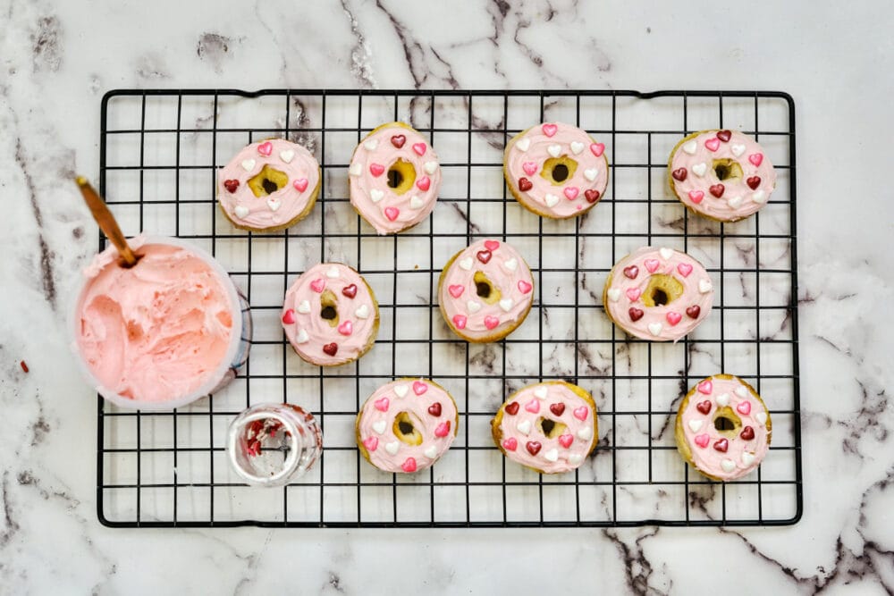 Frosted and sprinkled strawberry donuts on a wire rack.