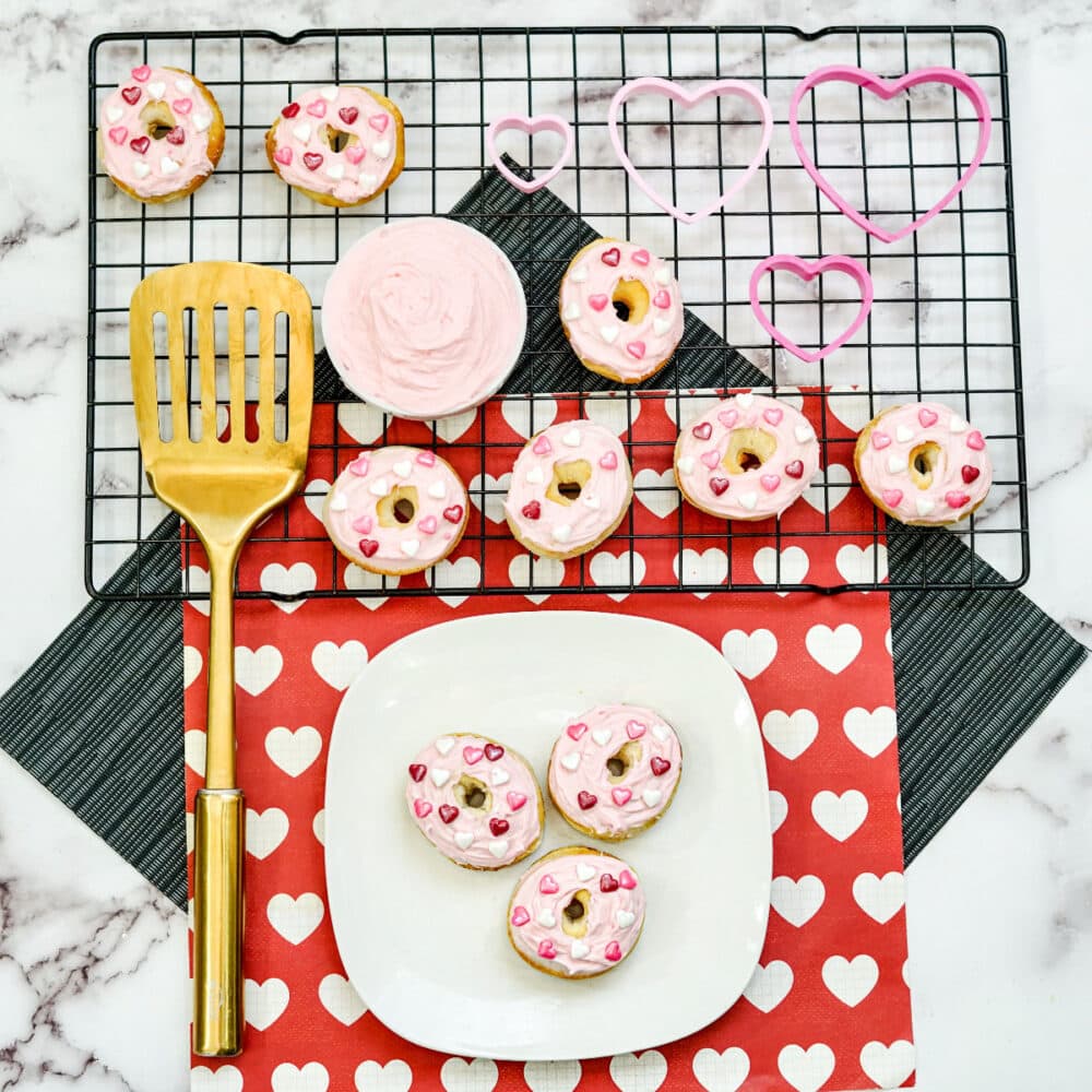 Frosted mini donuts on a plate and a rack next to a gold spatula.