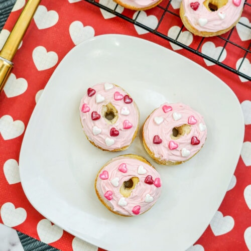 Three mini donuts on a plate next to a gold spatula.