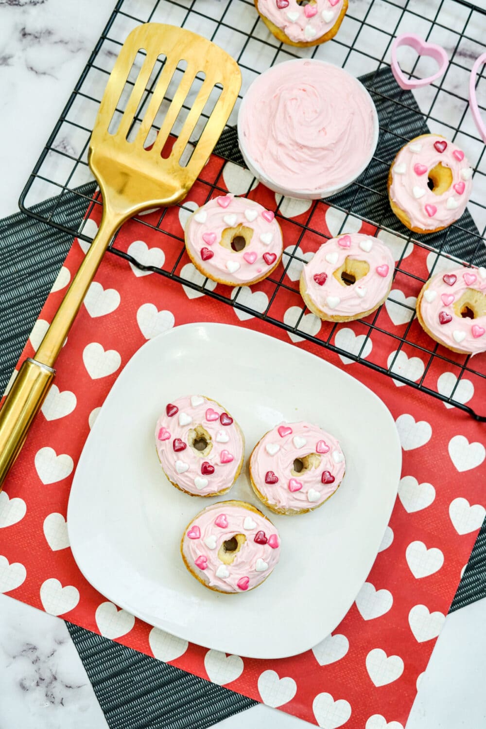 Pink frosted donuts on a plate and a rack.