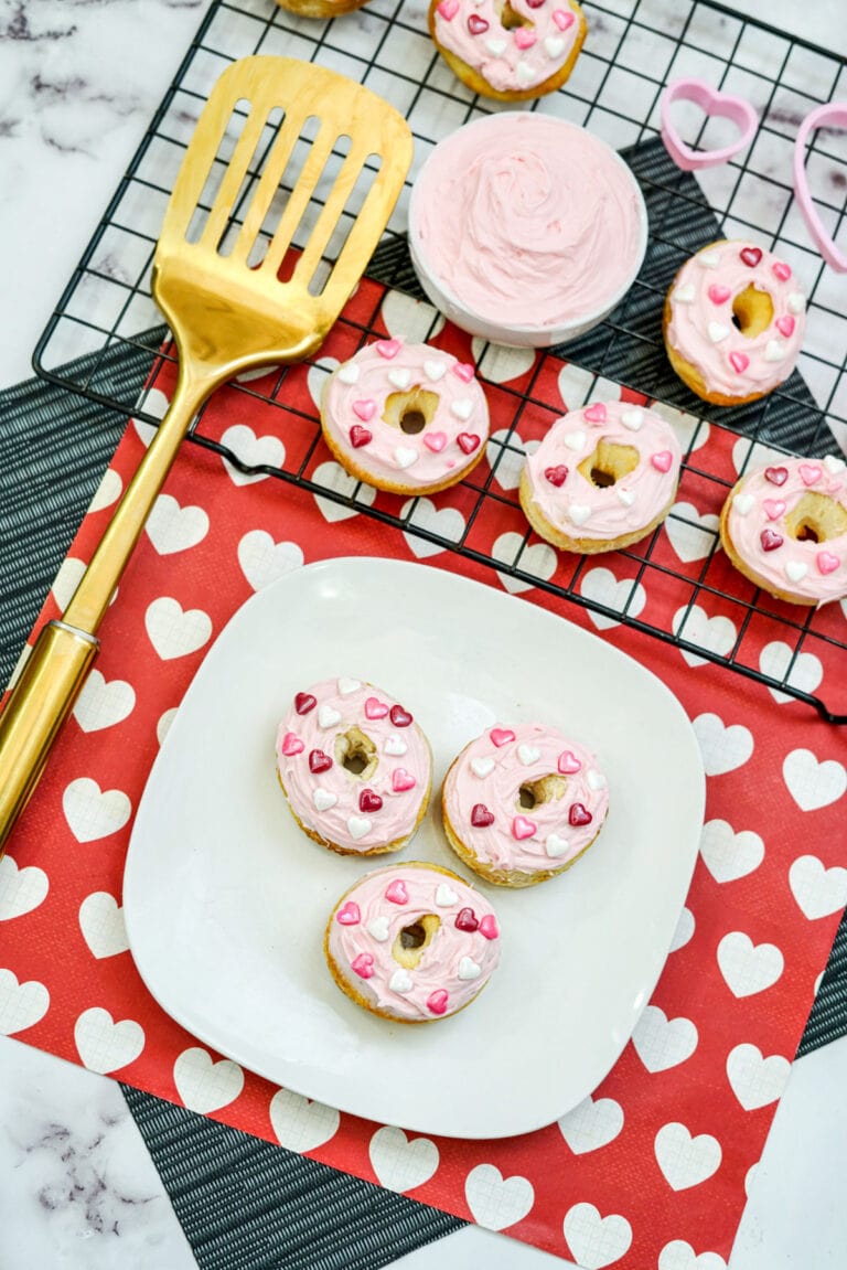 Mini strawberry donuts on a plate with more on a wire rack.