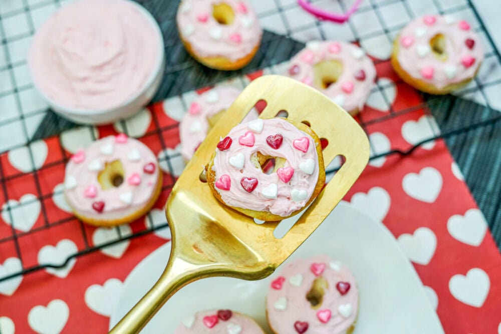 A gold spatula holding a strawberry mini donut above the rest of the donuts.