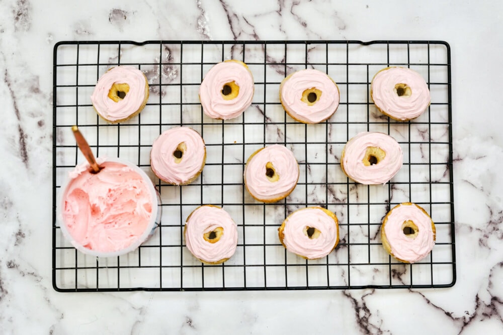 Adding strawberry frosting to mini donuts.