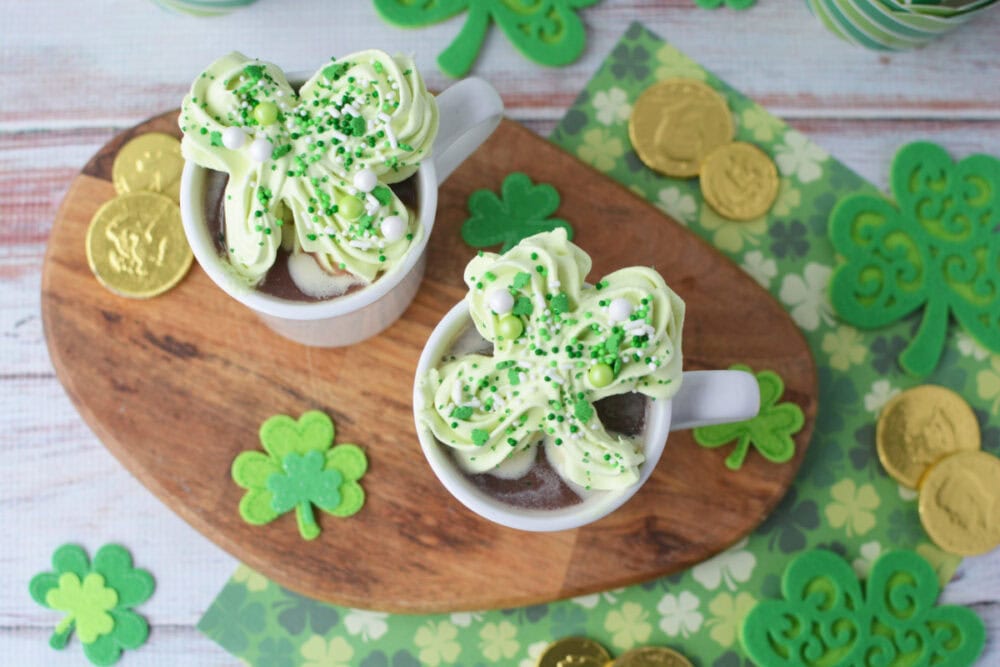 Two mugs of hot cocoa with whipped cream shamrocks on top.