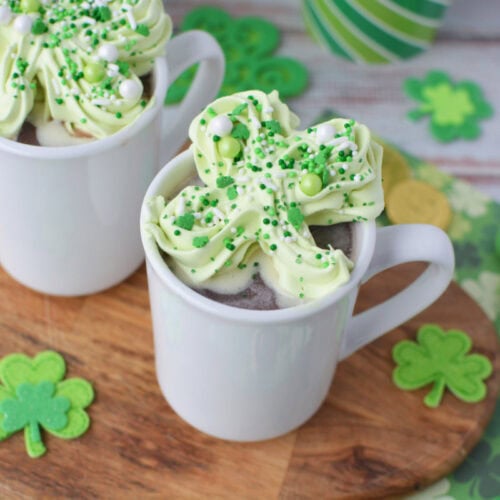 Frozen green shamrock whipped cream in mugs of hot chocolate.