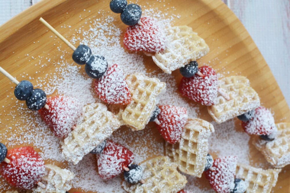 Mini waffles and berries on skewers topped with powdered sugar.