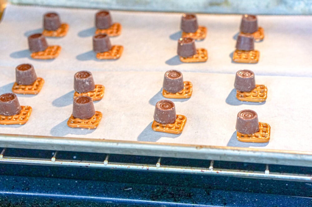 Pretzels topped with Rolo candies on a baking sheet.