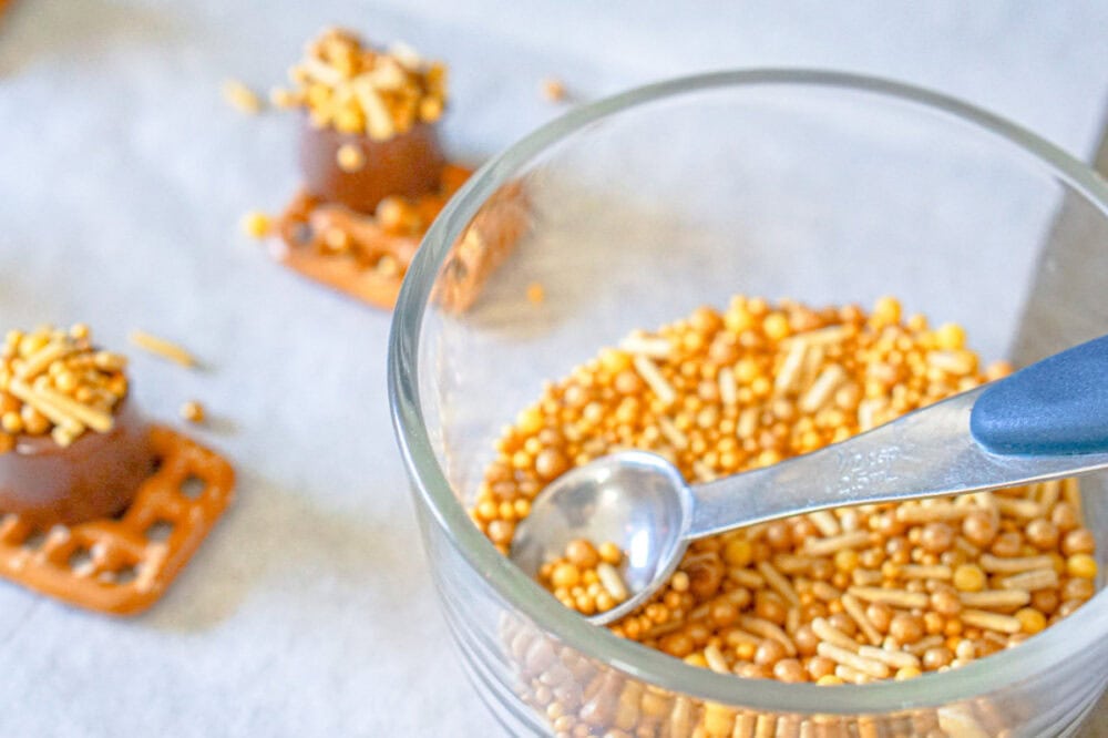 Adding gold sprinkles to Rolo candies on pretzels.