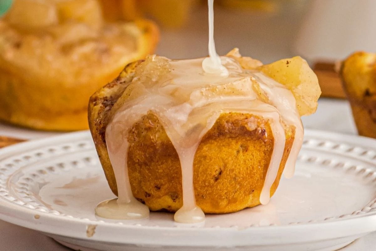 cinnamon roll apple pie cup with glaze being drizzled on