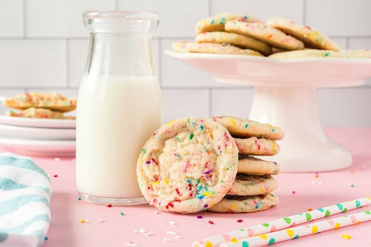 Confetti cookies stacked next to a glass of milk