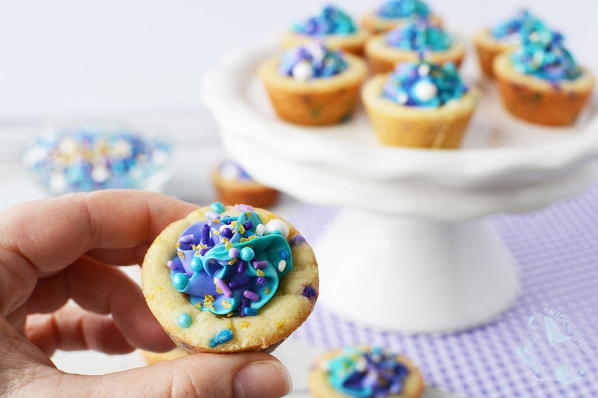 A hand holding a small cookie cup with blue and purple sprinkles