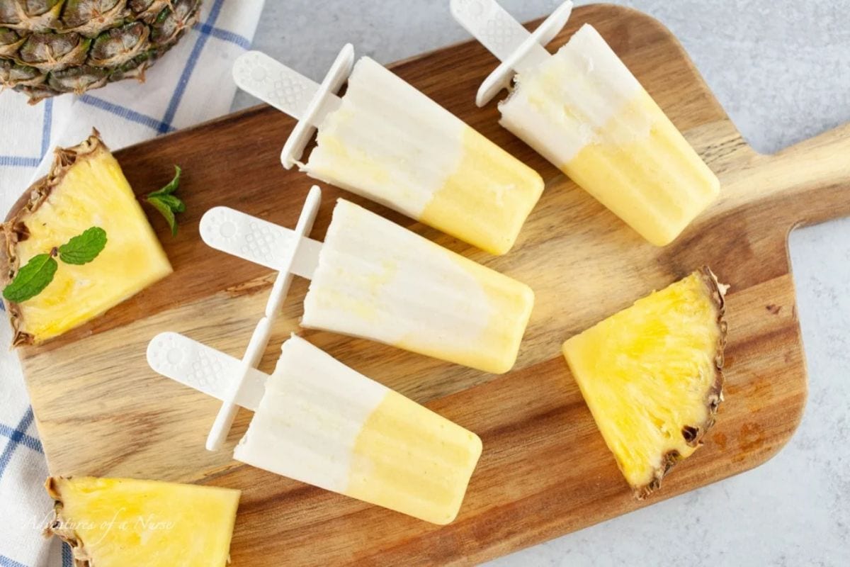 pina colada pops on a board with pineapple slices