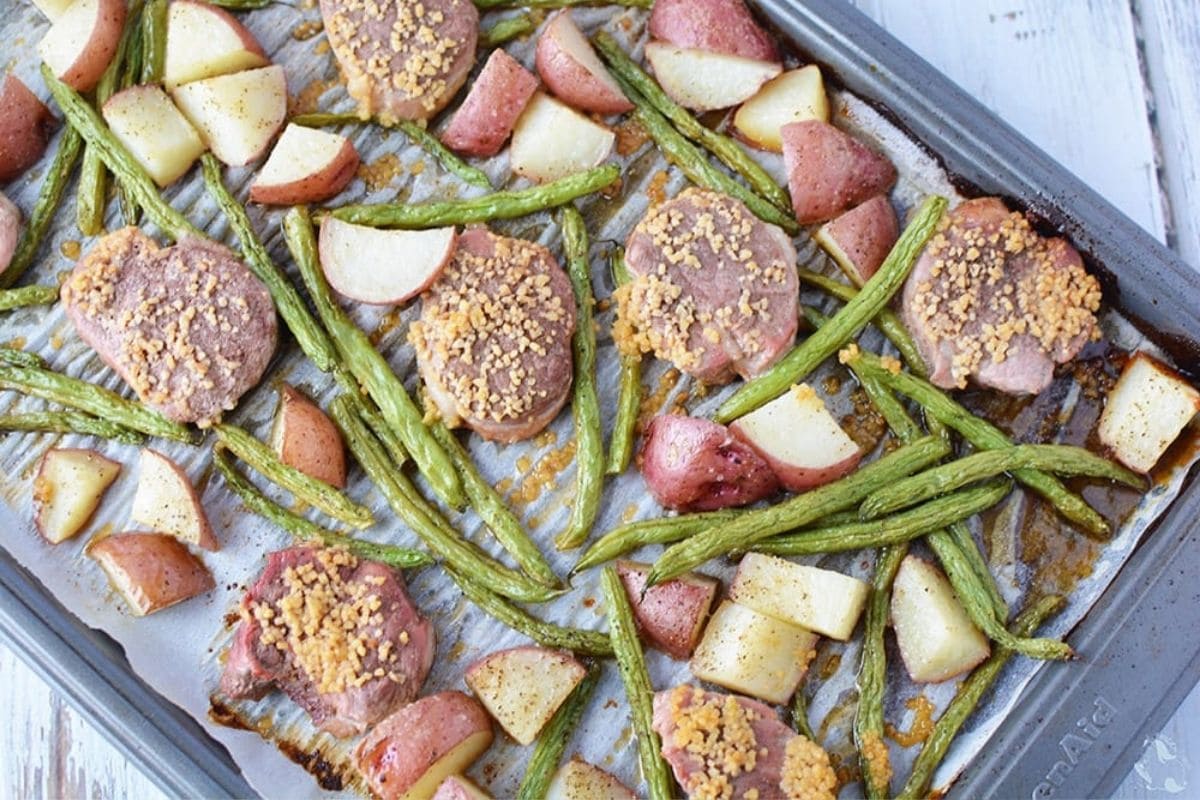 pork chops, potatoes, and green beans on a baking sheet