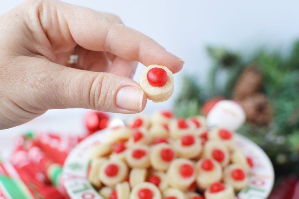 holding a shortbread cookie with a red candy in the middle