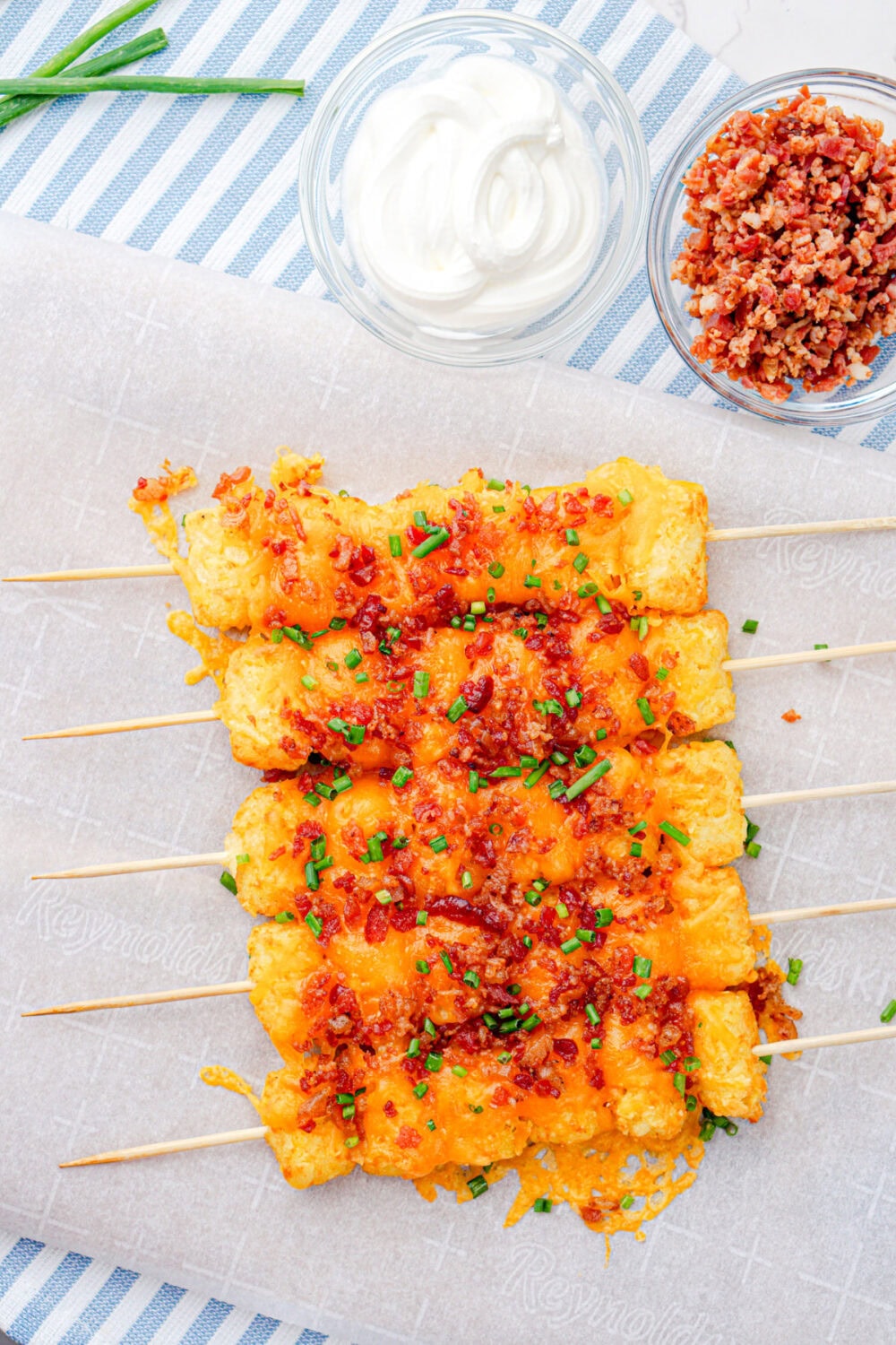 loaded tots on skewers next to bowls of sour cream and bacon