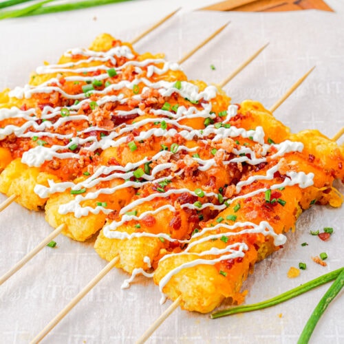 Loaded tater tots on skewers lined up on a table