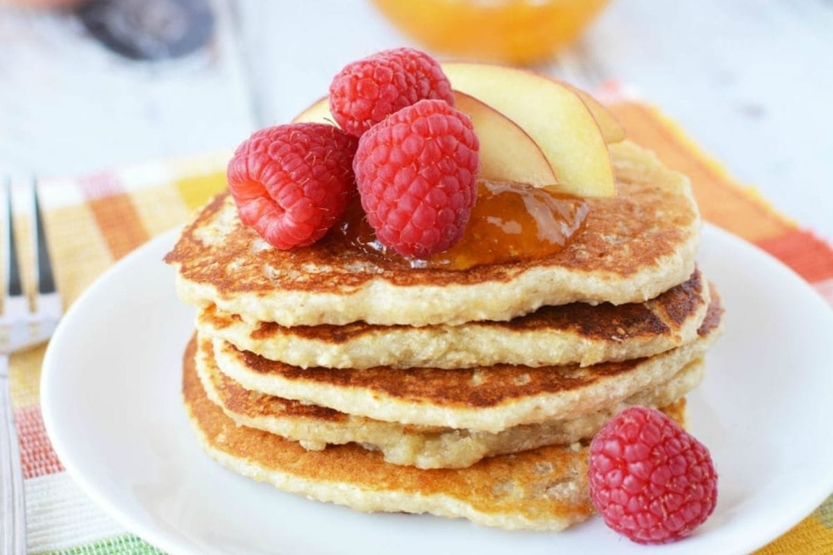 stack of pancakes topped with peach and raspberry