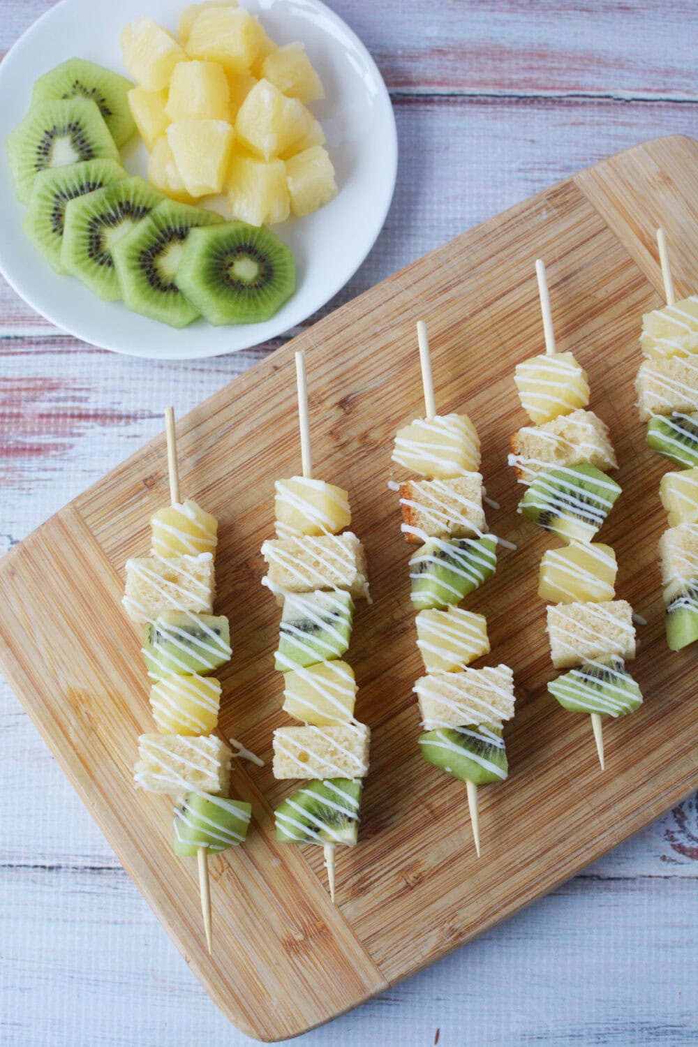 kiwi, pineapple, pound cake dessert skewers next to bowl of sliced fruit