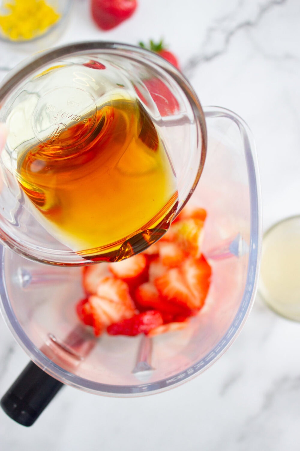 adding honey to a blender with strawberries